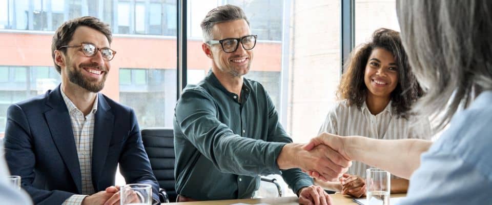 Four people sitting around a table, shaking hands.