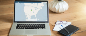 Image of a laptop on a desk with screen showing world map. Notebook and pen laying on the desk next to laptop.