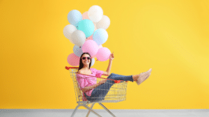 Female sitting in a shopping trolley holding a bunch of balloons.